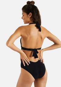 Sort bikini med halterneck-design, der er bundet i ryggen, og højtsiddende bund. Fremstillet af glat materiale med minimalistisk stil.