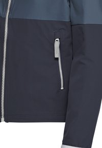 Μανίκι και εμπρός μέρος σκούρου μπλε μπουφάν με γκρι φερμουάρ και λεπτομέρεια με φερμουάρ σε τσέπη πάνω σε λείο ύφασμα.