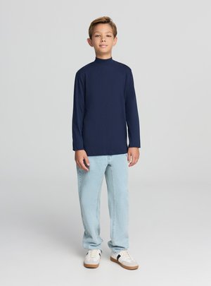 Camicia a maniche lunghe color blu marina con collo alto, abbinata a jeans azzurri a taglio dritto e sneakers bianche con dettagli neri.