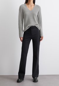 Maglione a costine grigio chiaro con scollo a V, indossato con pantaloni a gamba larga neri e scarpe nere, che enfatizzano un look casual e stratificato.