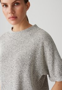 Lichtgrijs textuur t-shirt met korte mouwen, een losse pasvorm en een hoge halslijn. De stof heeft een subtiel gespikkeld patroon.
