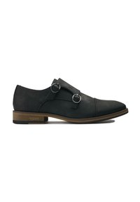 Black vegan leather shoe with two buckle accents and a pointed toe, featuring a medium brown heel and textured surface.