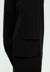 Gros plan d'un pantalon noir avec une grande poche latérale sur la cuisse, montrant la texture du tissu et les détails des coutures.
