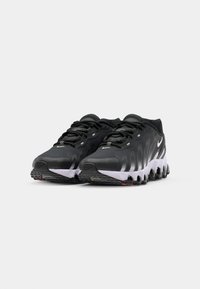 Zwarte sportieve schoenen met een gestructureerde bovenkant, golvende design, witte zool en onderscheidende zwarte rubberen accenten op de onderkant.