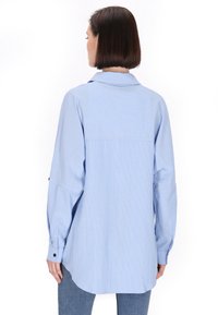 Camicia a maniche lunghe a righe blu con colletto all'italiana, vestibilità rilassata e orlo arrotondato. Presenta toppe sulle spalle e polsini con bottoni.