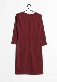 Une robe bordeaux à manches longues et longueur genou suspendue sur un cintre noir contre un fond blanc, le dos tourné vers l'avant.