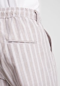 Pantalones de rayas beige claro con rayas verticales blancas, con una cintura elástica y un detalle de bolsillo lateral.