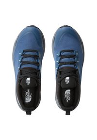 Zapatillas deportivas azules con detalles negros, parte superior de malla, superficie texturizada y cordones planos. Presenta un logotipo en la lengüeta y una pestaña en el talón.
