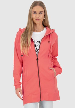 Sweatshirt à capuche corail avec fermeture éclair intégrale, deux poches latérales, manches côtelées et accent de logo en forme de cœur. Superposé sur un t-shirt graphique blanc.