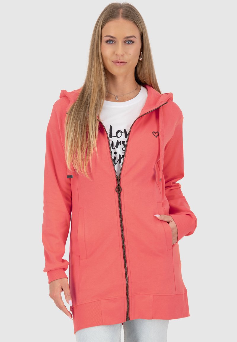 Felpa con cappuccio corallo con zip completa, due tasche laterali, polsini a costine e accento di logo a forma di cuore. Indossata sopra una t-shirt bianca con grafica.