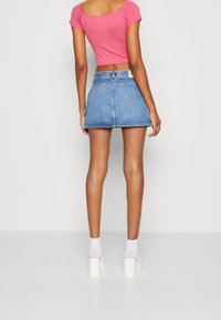 Růžový cropped top spárovaný s modrou denimovou sukní. Sukně má vysoký pas a je po kolena. Součástí jsou bílé platformové sandály a ponožky.