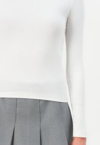 White ribbed long-sleeve top with a fitted design, paired with a pleated gray skirt. Smooth texture, minimal detailing.