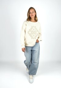 Cremetfarbener Sweatshirt mit strukturiertem Blumenmuster auf der Vorderseite, kombiniert mit hellblauen weit geschnittenen Jeans und weißen Sneakers. Glattes Material, lässige Passform.