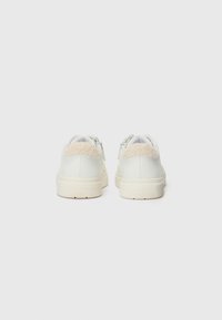Baskets blanches avec une finition en cuir lisse, des accents de fourrure beige douce au talon et une semelle en caoutchouc texturée. Branding subtil au talon.