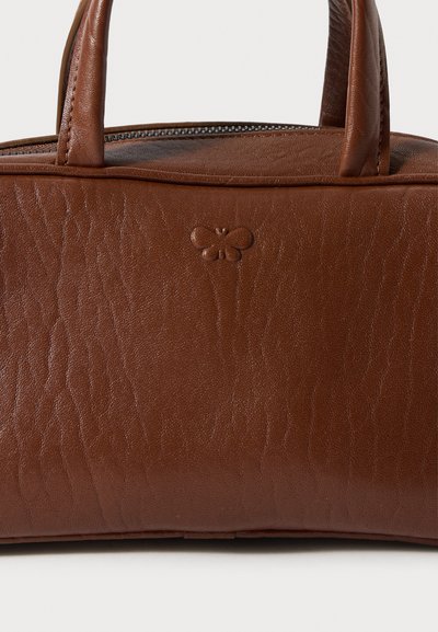 Barna bőrtáska, texturált felülettel, rövid fogantyúkkal és cipzáras záródással. Dombornyomott pillangó logó a táska elejének közepén.