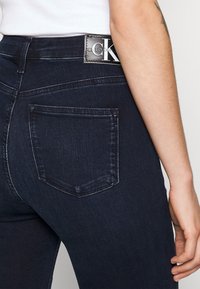 Dunkelblaue Jeans aus Denim mit hoher Taille, gerader Passform und einer Gesäßtasche mit einem Calvin Klein-Logo auf einem schwarzen Lederpatch.