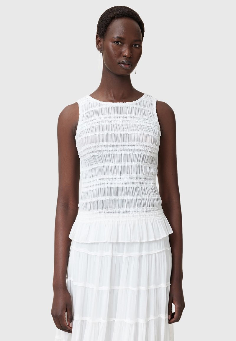 Top bianco senza maniche con texture arricciata, caratterizzato da un ruffle a peplum all'orlo e un collo liscio. Realizzato in tessuto leggero e trasparente.