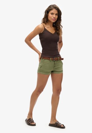 Brun tanktop med blonder, grønne shorts, flettet brun bælte og brune sandaler. Modellen står i en afslappet positur.