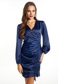 Rochie din satin bleumarin cu decolteu în V, mâneci lungi tip bufantă și plissare laterală. Dispune de șnururi ajustabile la margine pentru personalizarea potrivirii.