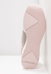 Semelle de sneaker Michael Kors beige et rose clair avec motifs géométriques texturés et nom de la marque sur le talon.