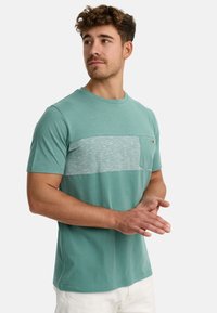 Kortærmet t-shirt i teal med en struktureret grå brystpanel og en lille lomme. Blødt bomuldsstof med rund halsudskæring.