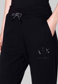 Zwarte sweatpants met een verstelbare tailleband, zijzakken en een reflecterende logo op de dij. Zacht materiaal met een gladde textuur.