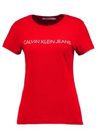 Red cotton t-shirt featuring a crew neckline and short sleeves. The front displays "CALVIN KLEIN JEANS" in bold white letters.