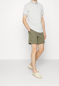 Randig grå polo med krage, ihop med olivgröna shorts och ljusa espadrillos, vilket skapar en avslappnad outfit.