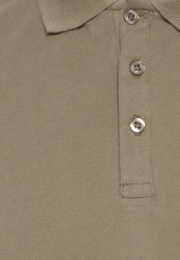 Khaki polo skjorte med tekstureret stof, der har en krave og tre metal knapper langs stolpen.