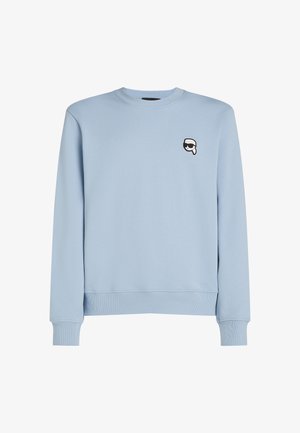 Jasnoniebieska bluza z miękkiej bawełny. Posiada okrągły dekolt oraz ściągacze na rękawach, a na piersi znajduje się małe czarno-białe logo graficzne.