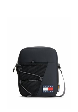 Kleine schwarze Umhängetasche mit vorderer Mesh-Tasche, verstellbarem Riemen und Tommy Jeans Logo-Patch an der unteren Ecke.