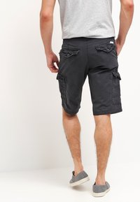 Pantalones cortos de carga gris oscuro hechos de algodón con múltiples detalles de bolsillos, de largo hasta la rodilla y un ajuste relajado, combinados con zapatos gris de slip-on.