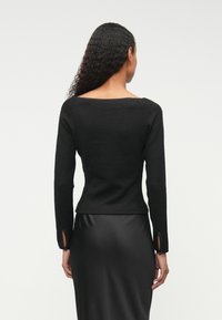 Top preto com nervuras de manga longa, com um decote largo e punhos abertos, combinado com uma saia preta lisa. Apresenta um tecido texturizado e um design ajustado.