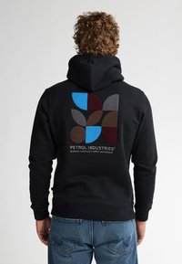 Černá mikina s kapucí, která na zádech obsahuje vícebarevný geometrický design v hnědé, modré, burgundské a šedé barvě, s potiskem loga.