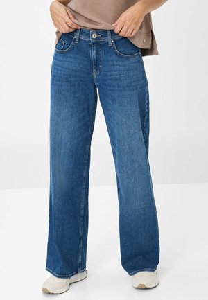 Blaue weit geschnittene Jeans aus Denim mit einem klassischen Fünf-Taschen-Design, ausgestattet mit einem Knopf- und Reißverschluss, getragen mit einem beigen Oberteil.