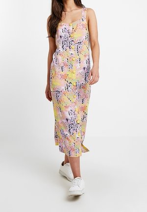 Robe midi sans manches dans des couleurs pastel avec des motifs abstraits, dotée de boutons sur le devant et d'une fente sur le côté, associée à des baskets blanches.