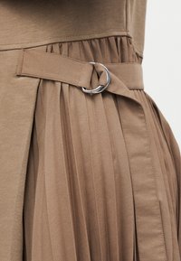 Gros plan sur un tissu plissé beige avec une ceinture assortie maintenue par une boucle à double anneau argentée à la taille.