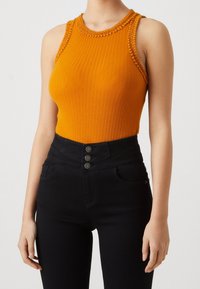 Orange ribbad bodysuit med hög halsringning och virkade detaljer vid axlarna. Sammanvävd med högmidjade svarta jeans med knapprar.