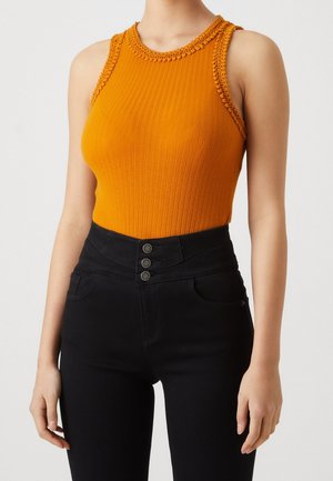 Bodysuit orange côtelé avec un col haut et des détails en crochet aux épaules. Associé à un jean noir taille haute avec des accents de boutons.