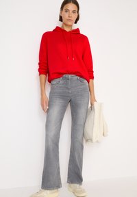 Felpa rossa con cappuccio e stringhe, jeans grigi a zampa d'elefante e sneakers di colore chiaro. Materiale morbido e tessurizzato; vestibilità informale; dettagli minimi.