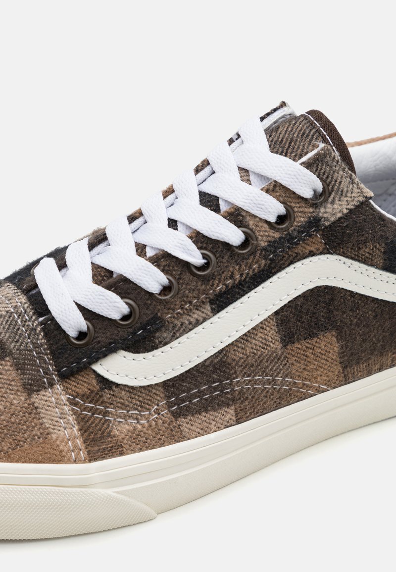 Baskets en toile à carreaux marron avec des lacets blancs, une bande en cuir crème et un dessus texturé, dotées d'une semelle en caoutchouc.