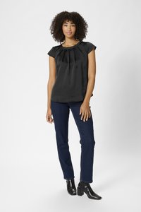 Blouse en satin noir avec des manches courtes, design plissé, associée à un jean bleu foncé et des bottines. Texture lisse et coupe ajustée.