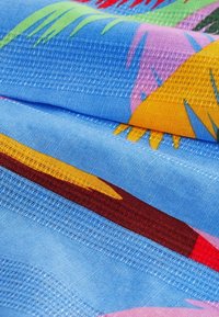Gros plan sur un tissu bleu avec des motifs de feuilles tropicales multicolores et des détails de couture tissée texturée.