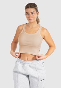 Top corto rigato beige con spalline larghe, design aderente e tessuto testurizzato. Il modello lo indossa con pantaloni della tuta grigi, mostrando il ventre.