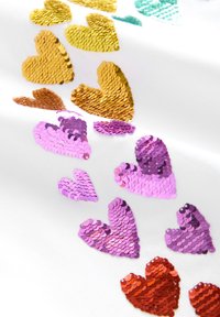 Ornementation en sequins sur tissu blanc, présentant des formes de cœurs éclatantes en or, orange, rose et turquoise. Surface brillante et texturée.