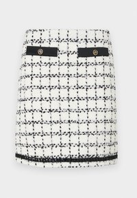 Tweed mini skirt in white and black, featuring a grid pattern, black accents, two front pockets, and gold button details.