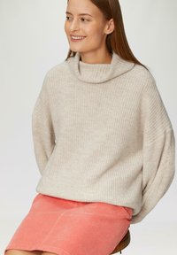 Lichtbeige, textuur gebreide trui met een col, gecombineerd met een perzikkleurige corduroy rok. De trui heeft raglanmouwen en een relaxte pasvorm.