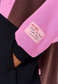 Bluza w kolorach blokowych: różowym, brązowym i czarnym. Posiada naszywkę na rękawie z tekstem. Wykonana z miękkiego materiału, z ściągaczami na rękawach.