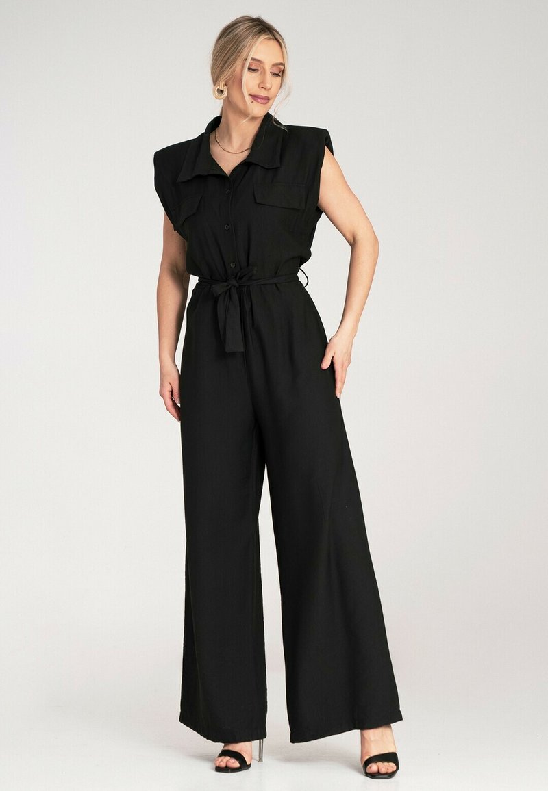 Czarny kombinezon z krótkimi rękawami w formie peleryny, z buttonem z przodu, dwoma kieszeniami na piersi oraz związanym w pasie. Szerokie nogawki i gładka tekstura.