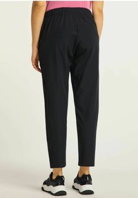 Czarne spodnie sięgające kostek z elastycznym pasem, bocznymi kieszeniami i gładką fakturą, w połączeniu z czarno-białymi trampkami.